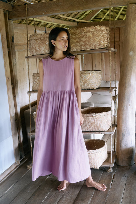 Nadi Dress Mauve — full length front view in rustic wooden interior with woven baskets, mauve double gauze cotton midi dress with gathered waist, natural bamboo shelving | Daughters of India