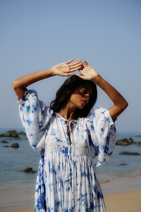 Kyra Midi Dress Deep Sea — close-up seated on beach rocks, deep sea shibori tie-dye cotton midi dress, V-neckline and gathered empire waist detail, coastal Goa India | Daughters of India